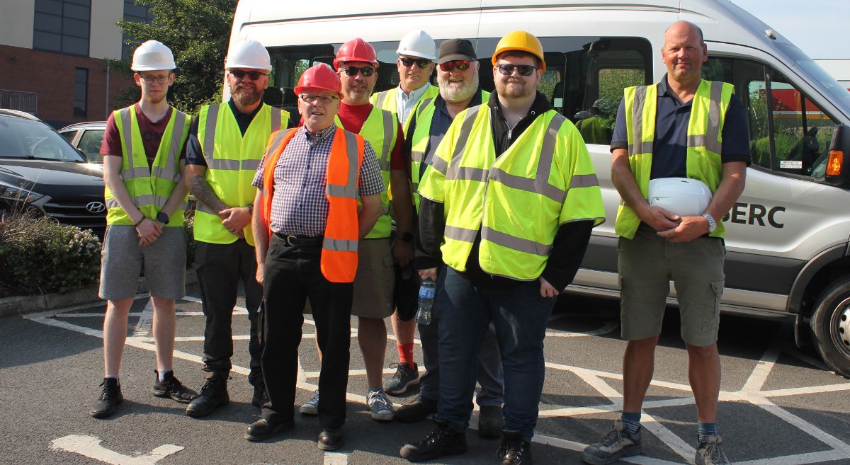 Eight men in high viz jackets with hard hats pictured in front of SERC mini bus